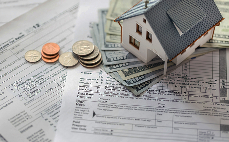 Miniature house with money on tax papers
